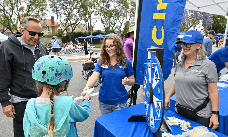 families cycling, children at UC Irvine booth, community members laughing with soap bubbles, UC Irvine vice chancellor Sherry Main receiving recognition from the city with the councilmembers