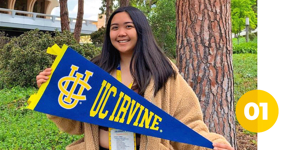 A smiling Asian female student holding a UC Irvine felt flag posing on campus
