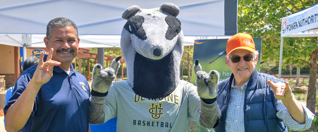 councilmember Larry Agran posing next to Peter the Anteater and UCI staff, all three making Zot sign