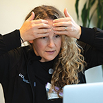 Person with hands on forehead practicing acupressure while looking at laptop.