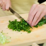 Close-up of person's hands chopping parsley with a knife.