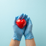 A person with surgical gloves with open hands holding a heart-shaped stress ball.