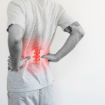 A person with their hands on their hips and a red-illuminated image of the person's lower spine.