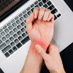 Person holding their wrist in pain while hovering over a laptop.