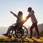 A caregiver pushing a person sitting in a wheelchair.